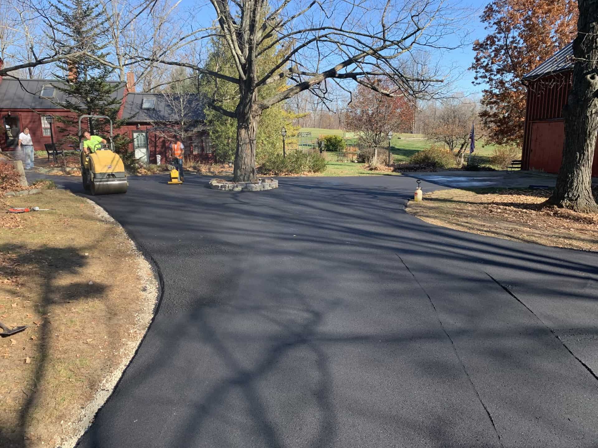 Crew rolling fresh asphalt millings on a curved driveway
